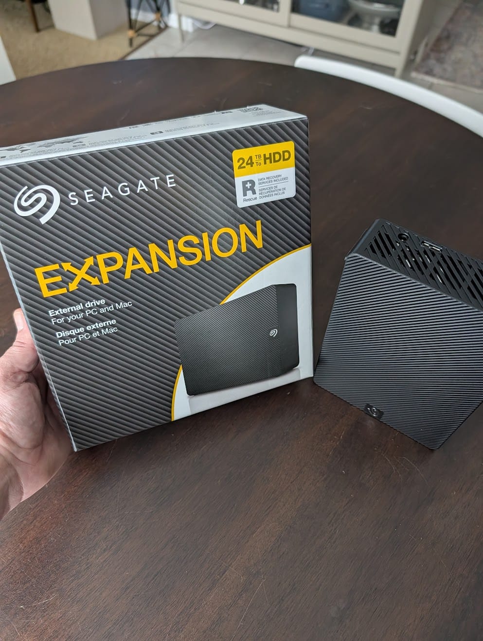 Hand holding a Seagate Expansion 24TB external hard drive box next to a Synology NAS unit