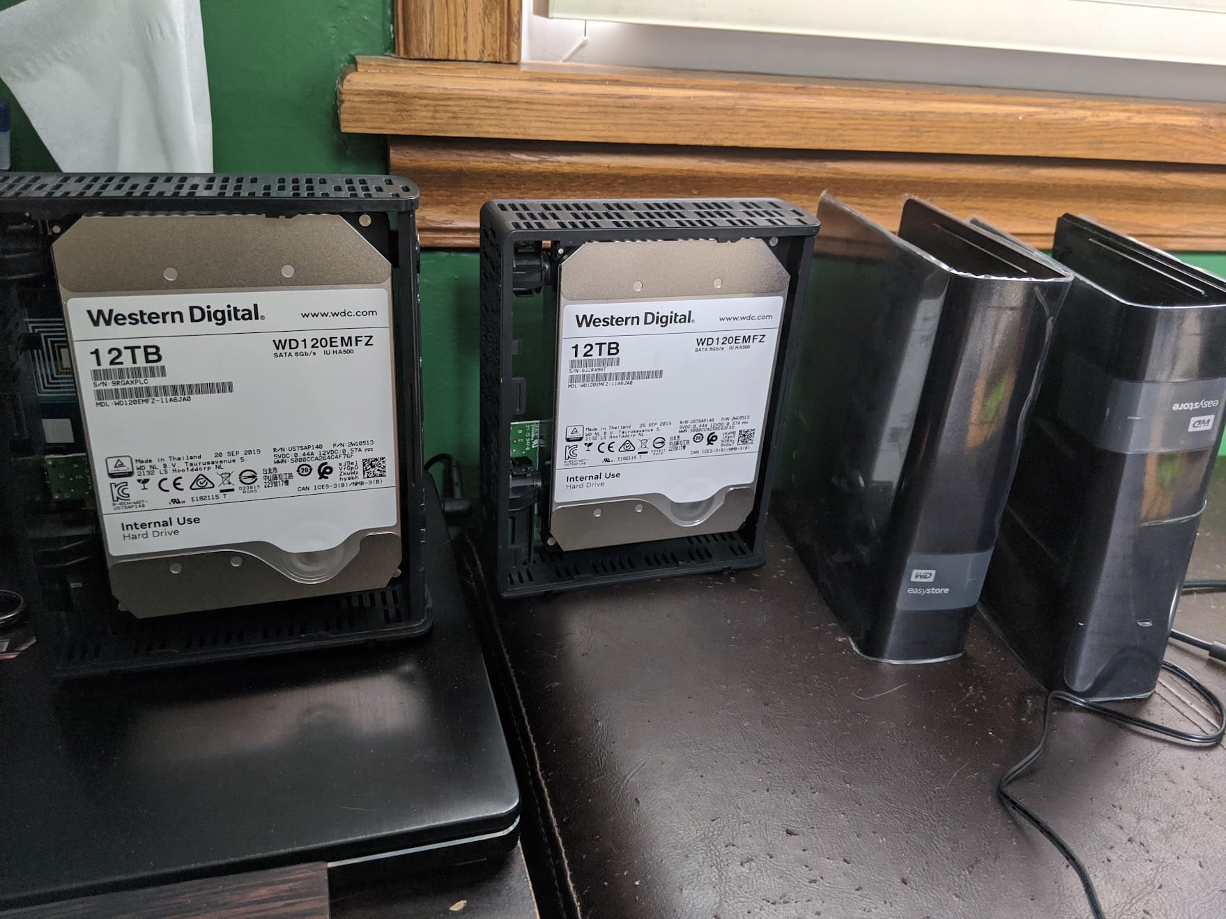Two Western Digital 12TB WD120EMFZ drives removed from their external enclosures, sitting on a desk next to the empty WD EasyStore shells