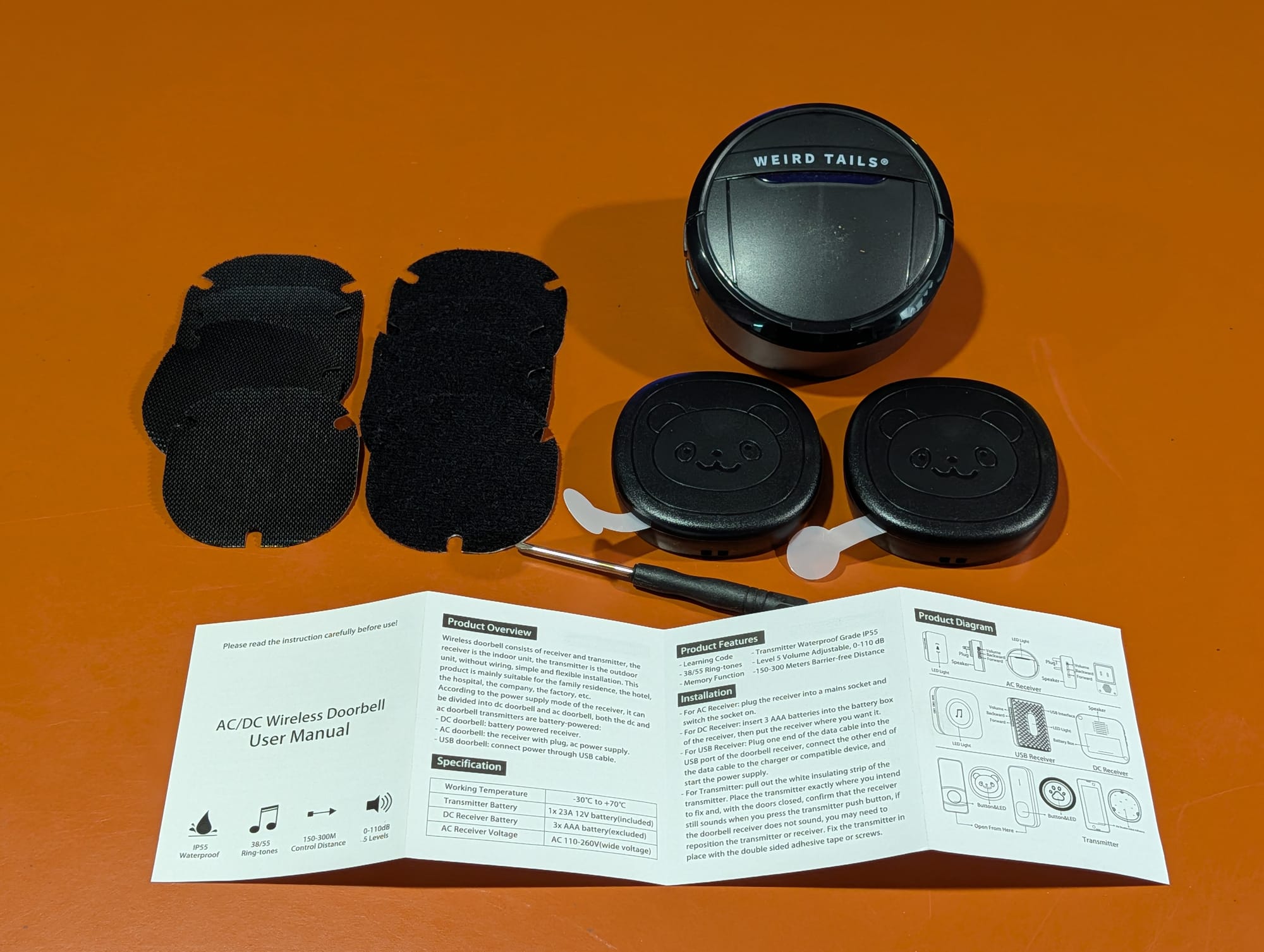The wireless doorbell kit unboxed: a plug-in chime receiver, two paw-print transmitter buttons, adhesive pads, a screwdriver, and the manual