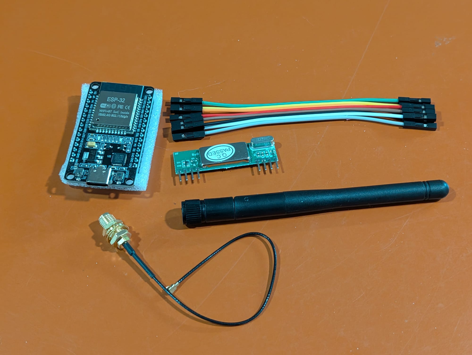 An ESP32 dev board, an RXB6 433 MHz receiver module, jumper wires, and a small whip antenna laid out on a desk